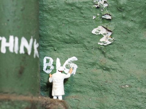 Miniaturmännchen vor grünem Hintergrund, das Think Big an die Wand schreibt